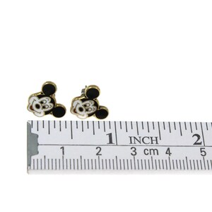 May include: A pair of gold-toned stud earrings featuring a Mickey Mouse design. The earrings have black and white enamel details. The ruler shows the earrings are approximately 0.5 inches in size.