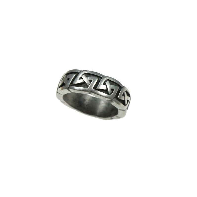 K&ouml;nnte beinhalten: Ein silberfarbener Ring mit einem sich wiederholenden keltischen Knotenmuster. Der Ring hat ein Band mit einer Reihe von miteinander verbundenen geometrischen Formen, die ein durchgehendes Muster bilden. Der Ring ist vor einem wei&szlig;en Hintergrund platziert.