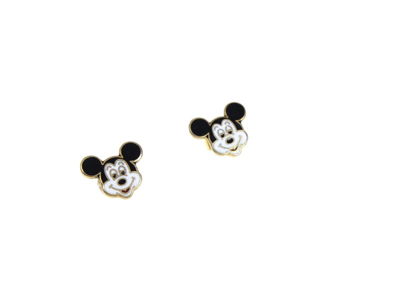 May include: Two gold-toned Mickey Mouse face stud earrings. Each earring features a black head with white facial features and a gold border. The earrings are set against a white background.