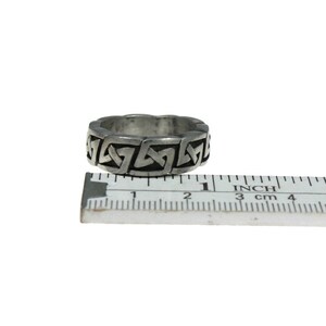 K&ouml;nnte beinhalten: Ein silberfarbener Ring mit einem keltischen Knotenmuster. Der Ring ist etwa 2 cm breit. Ein Lineal mit Zoll- und Zentimetermessungen liegt daneben.