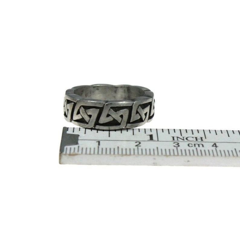 K&ouml;nnte beinhalten: Ein silberfarbener Ring mit einem keltischen Knotenmuster. Der Ring ist etwa 2 cm breit. Ein Lineal mit Zoll- und Zentimetermessungen liegt daneben.
