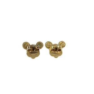 May include: A pair of gold-colored stud earrings, each shaped like a mouse head with round ears. The earrings are shown from the back, revealing the post and backing mechanism. The design is simple and elegant.