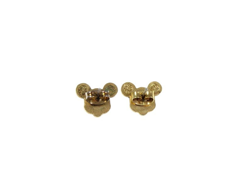 May include: A pair of gold-colored stud earrings, each shaped like a mouse head with round ears. The earrings are shown from the back, revealing the post and backing mechanism. The design is simple and elegant.