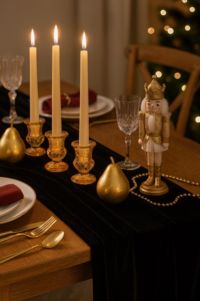 K&ouml;nnte beinhalten: Festliche Tischdekoration mit brennenden Kerzen in bernsteinfarbenen Glashaltern, goldenen Birnen und einem dekorativen Nussknacker. Der Tisch ist mit Tellern, Besteck und Weingl&auml;sern auf einem schwarzen Tischl&auml;ufer gedeckt.