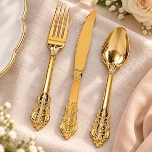 May include: A set of three gold-colored utensils including a fork, a serrated knife, and a spoon. Each piece features a highly reflective, polished finish and an intricate, embossed floral pattern along the handle and the neck of the utensil.