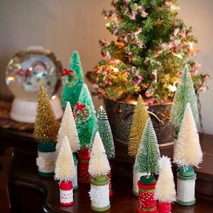 May include: A collection of miniature Christmas trees in various colors and styles. Some are green, gold, and white, with decorative bases. A snow globe and a larger potted tree are also present, creating a festive holiday display.
