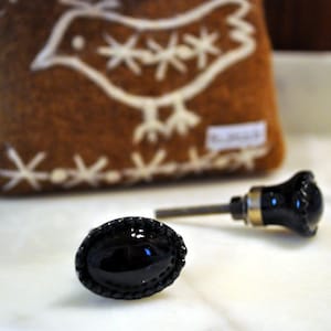 Könnte beinhalten: Zwei schwarze Schrankknöpfe mit einem dekorativen, perlenbesetzten Rand. Ein Knopf ist an einem silbernen Metallstiel befestigt.