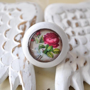 Könnte beinhalten: Weißer Keramik-Knopf mit einem runden, klaren Glaseinsatz, der ein Vintage-Blumendesign mit einer rosa Rose und grünen Blättern zeigt.
