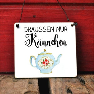 Könnte beinhalten: Ein weißes Holzschild mit schwarzem Text, der "Draussen nur Kännchen" lautet, und einer blauen Teekanne mit roten Rosen darauf.