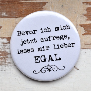 Könnte beinhalten: Weißer runder Knopf mit schwarzem Text, der lautet "Bevor ich mich jetzt aufrege, ist es mir lieber EGAL".