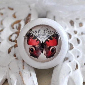Könnte beinhalten: Weißer runder Knopf mit einem Vintage-Postkarten-Design mit einem rot-schwarzen Schmetterling mit den Worten "Post Card" auf dem Knopf.