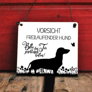Könnte beinhalten: Weißes rechteckiges Schild mit schwarzem Text und einer schwarzen Dackelsilhouette. Das Schild lautet "VORSICHT FREILAUFENDER HUND" und "Bitte das Tor geschlossen halten!". Ein Schmetterling und florale Akzente ergänzen das Design.