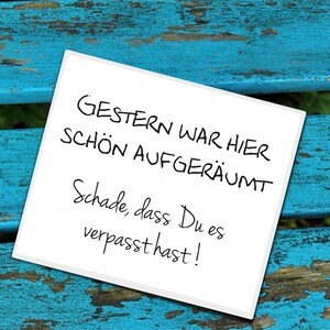 Könnte beinhalten: Ein weißer Zettel mit schwarzer handschriftlicher Aufschrift auf einer blauen Holzoberfläche. Der Text lautet "Gestern war hier schon aufgeräumt. Schade, dass du es verpasst hast!"