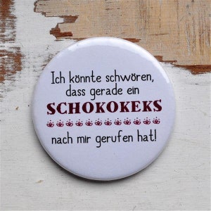 Könnte beinhalten: Runder weißer Knopf mit dem Text "Ich könnte schwören, dass gerade ein SCHOKOKEKS nach mir gerufen hat!" in rot und schwarzer Schrift.