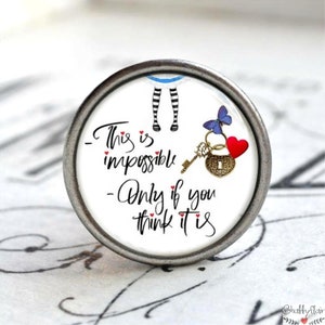 Könnte beinhalten: Runder, silberfarbener Knopf mit dem Zitat "This is impossible - Only if you think it is" in schwarzer Schrift. Der Knopf zeigt ein Alice im Wunderland-Thema mit Schlüssel, Herz und Schmetterling.