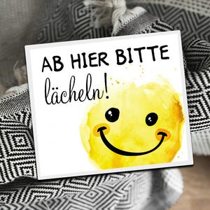 Könnte beinhalten: Ein weißes Schild mit schwarzem Text, auf dem "AB HIER BITTE lächeln!" steht, mit einem gelben Smiley-Gesicht mit Aquarell-Akzenten.