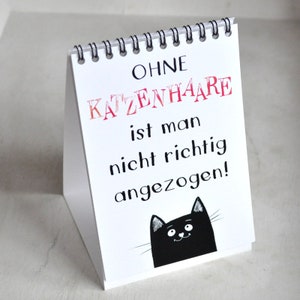 May include: White desk calendar with a black cat illustration and the text "OHNE KATZENHAARE ist man nicht richtig angezogen!"