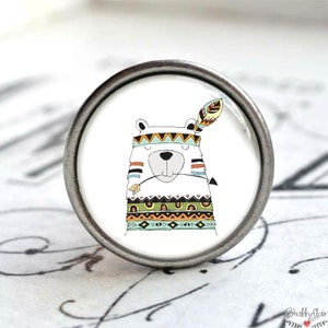 Könnte beinhalten: Ein weißer Bär mit einem bunten geometrischen Muster und einem Federkopfschmuck. Der Bär trägt ein Stirnband mit einem türkisfarbenen und weißen Muster. Der Bär hält einen kleinen Pfeil im Maul.