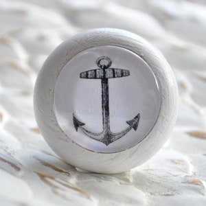 Könnte beinhalten: Weißer Holz-Knopf mit einem schwarz-weißen Anker-Design. Der Anker befindet sich mittig auf einem weißen Kreis mit schwarzem Rand.