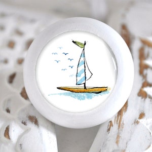Könnte beinhalten: Weißer Keramik-Knopf mit einem blau-weiß gestreiften Segelboot und Möwen auf einem blauen Aquarell-Hintergrund.