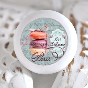 Könnte beinhalten: Runder weißer Knopf mit einem blauen und weißen Muster, das einen Stapel Macarons und den Text "Les Delices Paris" zeigt.