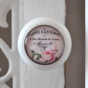 Könnte beinhalten: Weißer runder Knopf mit einem dekorativen Blumendesign und dem Text "Cafes & Legumes 6. Rue Mission de France Marseille" in Schwarz.