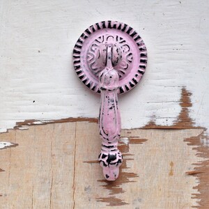 Könnte beinhalten: Rosa-schwarzer Metall-Schrankknauf mit dekorativem Design. Der Knauf hat eine runde Basis und einen langen, schlanken Griff.