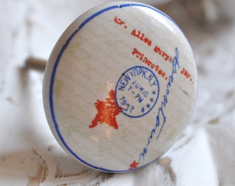 May include: White ceramic knob with a blue rim and a red star. The knob has a blue and white stamp that reads "NEW YORK, N.Y. JUNIG 7-PM 1937" and a handwritten inscription that reads "G. Allen Butz's Princeton, N.J."