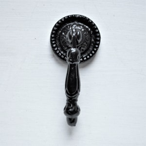 Könnte beinhalten: Schwarzer Türknauf aus Metall mit einer dekorativen runden Platte und einem langen, verzierten Griff.