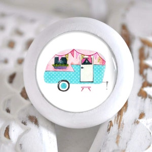Könnte beinhalten: Weißer Keramik-Knopf mit einer bunten Illustration eines Vintage-Wohnwagens mit rosa und blauen Akzenten und einer rosa-weißen Girlande.