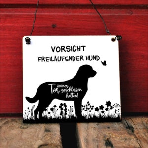 Könnte beinhalten: Ein weißes Holzschild mit schwarzem Text und einer schwarzen Silhouette eines Hundes. Das Schild lautet "Vorsicht Freilaufender Hund" und "Tor immer geschlossen halten!"