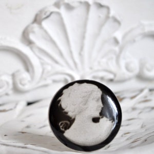 Könnte beinhalten: Ein schwarz-weißer Kameenring mit einem Porträt einer Frau. Der Ring ist in eine schwarze Metallfassung gefasst.