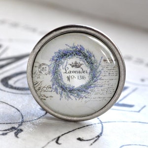 Könnte beinhalten: Ein silberner Knopf mit einer Glasoberfläche, die einen Kranz aus Lavendelblüten und den Text "Lavender No. 1316" zeigt.