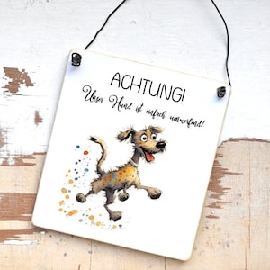 Könnte beinhalten: Ein weißes Schild mit schwarzem Text, auf dem "ACHTUNG! Unser Hund ist einfach unwiderstehlich!" steht. Ein Cartoon-Hund mit braunen und gelben Flecken rennt nach rechts. Der Hund hat einen fröhlichen Ausdruck und hinterlässt eine Spur aus bunten Punkten.