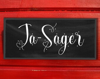 May include: A black chalkboard sign with white text that says "Ja-Sager" with small hearts and dots around the text.