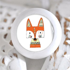 Könnte beinhalten: Weißer Keramik-Knopf mit einem bunten Comic-Fuchs, der einen geometrisch gemusterten Pullover trägt. Der Fuchs hat ein schwarzes Auge und ein weißes Auge mit einem schwarzen Punkt.