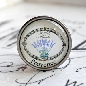 Könnte beinhalten: Ein silberner Knopf mit einer Glasoberfläche, die eine Illustration einer Lavendelblume und den Text "Lavendula Lavender Provence" zeigt.