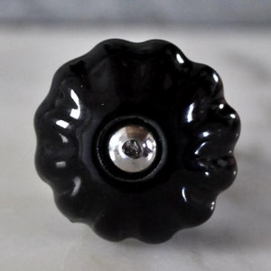 Könnte beinhalten: Schwarzer Keramik-Schrankknopf mit geriffeltem Design und silbernem Metallzentrum.