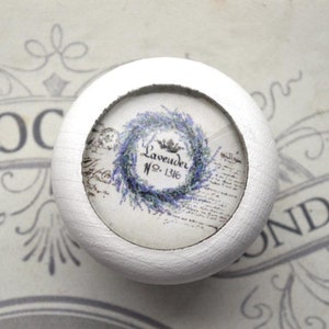Könnte beinhalten: Runder weißer Knopf mit einem Glaseinsatz, der ein Vintage-Blumendesign mit einem Lavendelkranz und dem Text "Lavender No. 1316" zeigt.