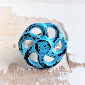 Könnte beinhalten: Ein blauer und schwarzer Metall-Schrankknauf mit einer abgenutzten Oberfläche. Der Knauf hat eine runde Form mit fünf Speichen.