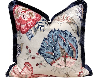 Puede incluir: Una almohada decorativa con un patrón floral que presenta flores rojas, azules y blancas sobre un fondo crema. La almohada tiene un ribete de flecos azul marino.
