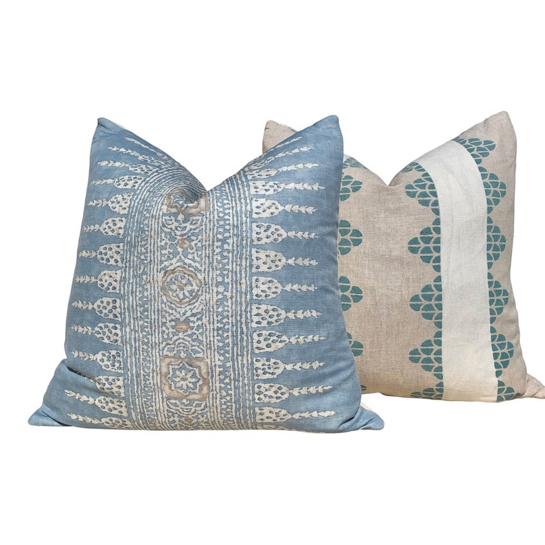 May include: Two decorative throw pillows. One is light blue with a cream and tan patterned design. The other is tan with a teal floral pattern and a white stripe. Both pillows have a square shape.