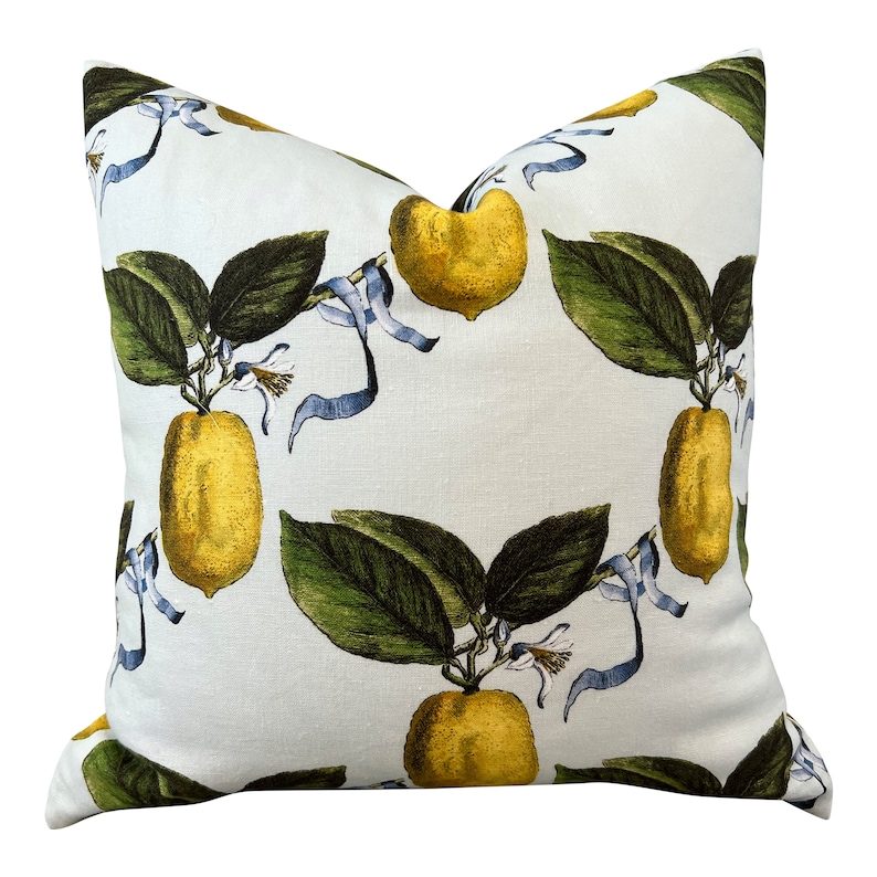 May include: Square throw pillow with a white background and a repeating pattern of yellow lemons, green leaves, and blue ribbons. The pillow has a soft, textured appearance, suitable for home decor.