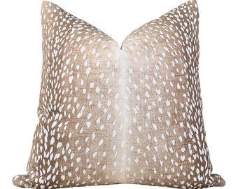 May include: A decorative throw pillow with a fawn-like pattern. The pillow features a light brown background with white spots, creating a spotted design. The pillow is square-shaped and has a soft, textured appearance, suitable for home decor.