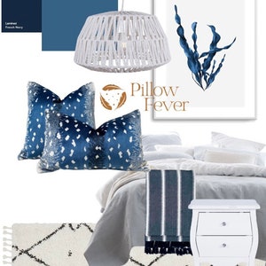 Pu&ograve; includere: Un letto bianco con biancheria da letto blu e bianca, un comodino bianco con due cassetti, una lampada a sospensione bianca intrecciata e un tappeto bianco con un motivo geometrico nero. Due cuscini decorativi blu e bianchi a motivi sono sul letto. Una stampa incorniciata con un disegno di alghe blu ad acquerello e il testo "Pillow Fever" &egrave; sul muro.