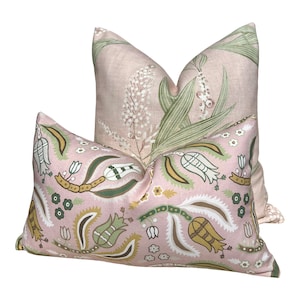 Op de afbeelding: Twee decoratieve kussens. Het voorste kussen heeft een roze achtergrond met een herhalend patroon van witte, groene en gele bloemen- en paisley-ontwerpen. Het achterste kussen heeft een roze achtergrond met een bloemmotief van witte bloemen en groene bladeren.