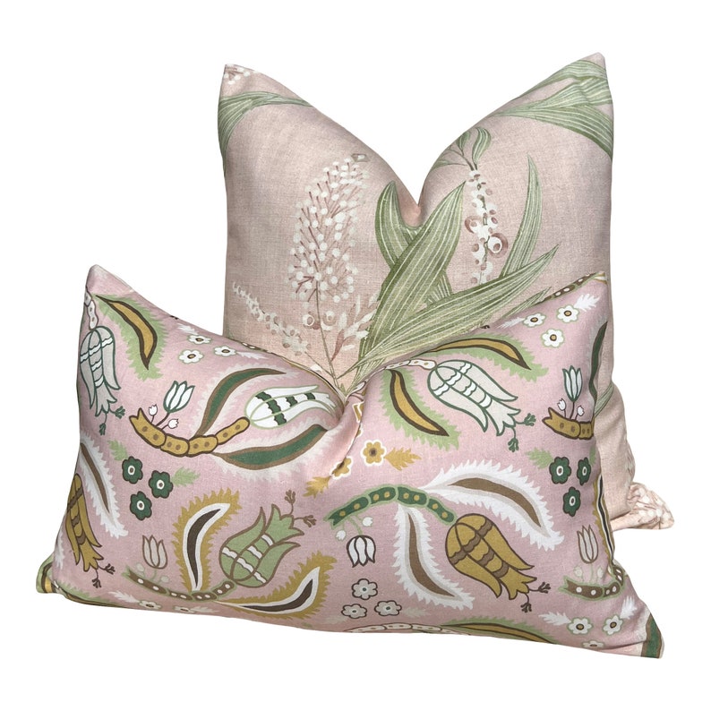 Op de afbeelding: Twee decoratieve kussens. Het voorste kussen heeft een roze achtergrond met een herhalend patroon van witte, groene en gele bloemen- en paisley-ontwerpen. Het achterste kussen heeft een roze achtergrond met een bloemmotief van witte bloemen en groene bladeren.