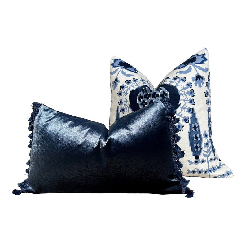 May include: Two decorative throw pillows with blue and white patterns. The pillow on the left is a solid dark blue velvet with a fringe trim. The pillow on the right is a white fabric with a blue floral pattern.