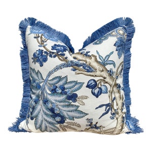 Pu&ograve; includere: Cuscino floreale blu e bianco con un bordo di frangia blu. Il cuscino presenta un design floreale stilizzato con foglie e fiori blu e marroni.