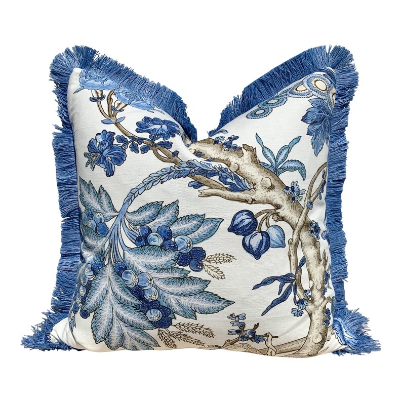 Pu&ograve; includere: Cuscino floreale blu e bianco con un bordo di frangia blu. Il cuscino presenta un design floreale stilizzato con foglie e fiori blu e marroni.